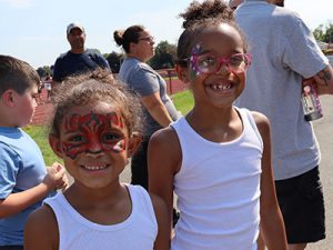Two siblings stand together looking at camera and smiling. The two children have face paint decorations around their eyes.