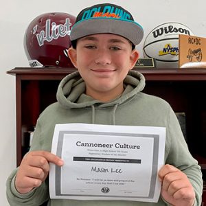 grade 7 student wearing a ball cap and smiling at camera holding Cannoneer Culture certificate for Being Present 