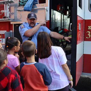 Students look inside a fire truck as a firefighter points to a piece of equipment.