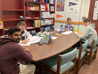 Students and college admissions counselors seated around a conference table looking up at camera and smiling.