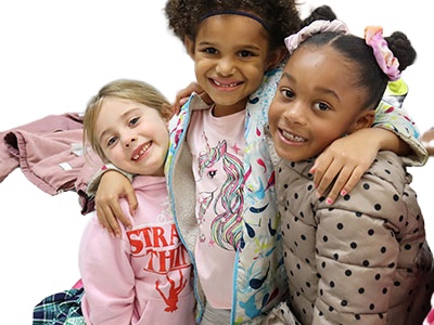 Three students seated together wearing pink clothing. The student in the middle has arms around the other two students. All are looking at the camera and smiling.