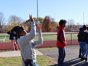 Student wearing fatal vision goggles looking up with hands ready to catch a ball as another student looks on.