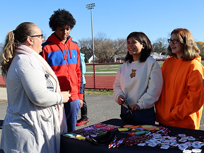 An Albany Stop DWI program coordinator speaks with three students standing at a display table with stop DWI pens, pencils and key chains.