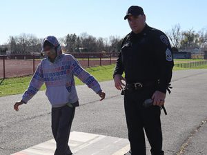 A student wearing fatal vision goggles walks a straight line as a Stop DWI officer stands nearby.