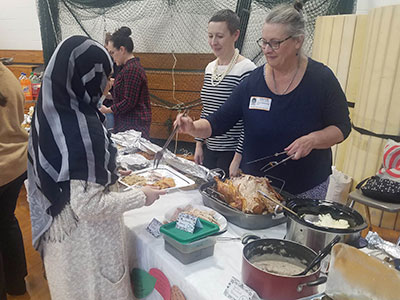 Teachers stand behind a table of food carving a turkey and placing food on a student's plate.