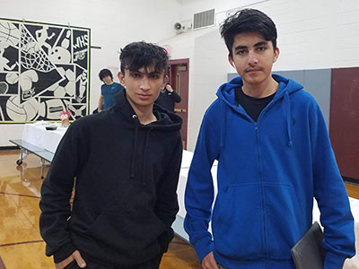 Two English languages learners stand next to each other looking and smiling at the camera.