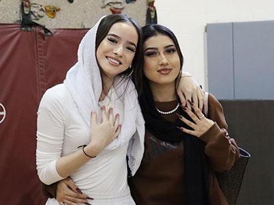 Two English language learners stand together arm-in-arm, smiling at the camera.