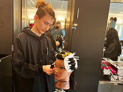 With a pair of scissors in hand, a student cuts hair on mannequin head.