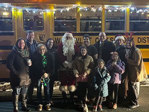 The superintendent stands in front of a decorated school bus with several school board members, students and staff