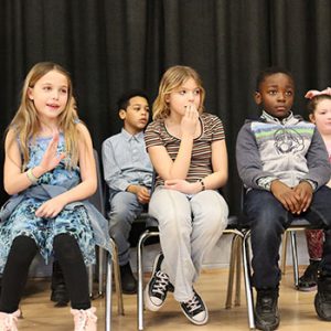 Spelling bee participants sit in chairs on the stage waiting for the competition to begin.