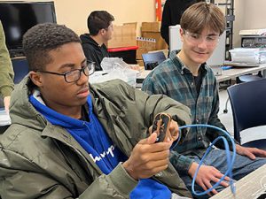 Watervliet High School student works with a cable and tools as another student seated nearby observes.