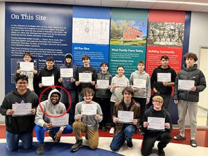 Fourteen Career and Technical Education students stand or kneel together in a group while holding documents that signify their Network Cabling Academy Fiber Certification. All are looking at the camera and smiling.