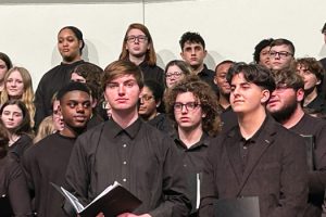 Watervliet High School student stands on stage holding a music book at the Albany Pro Musica High School Choral Festival.