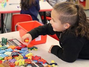 prekindergarten student at desk playing with block letters.