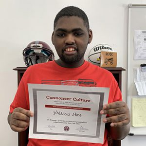 Grade 8 Student of the Month smiles at camera while holding Cannoneer Club Award Certificate