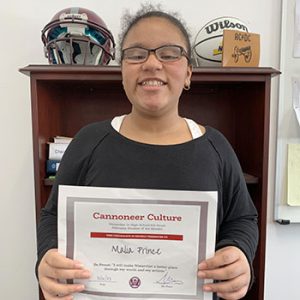 Grade 6 Student of the Month smiles at camera while holding Cannoneer Club Award Certificate