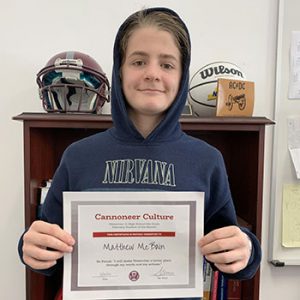 Grade 8 Student of the Month smiles at camera while holding Cannoneer Club Award Certificate