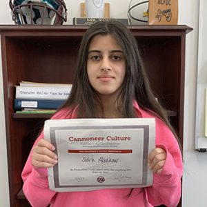 Grade 6 Student of the Month smiles at camera while holding Cannoneer Club Award Certificate
