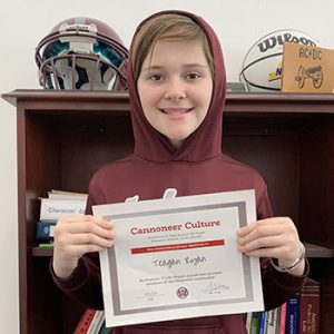 Grade 7 Student of the Month smiles at camera while holding Cannoneer Club Award Certificate