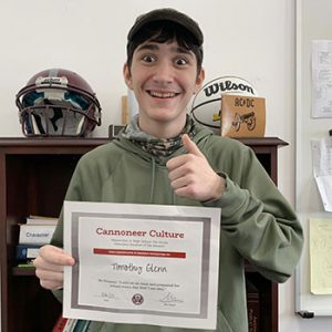 Grade 7 Student of the Month smiles at camera while holding Cannoneer Club Award Certificate
