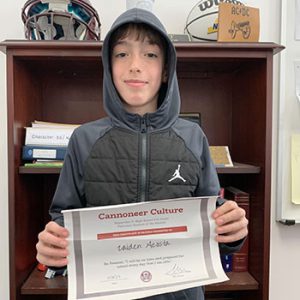 Grade 6 Student of the Month smiles at camera while holding Cannoneer Club Award Certificate