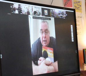 Author and news anchor appears on screen holding book to read to students.