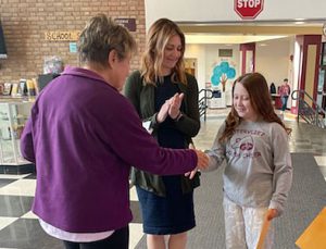 Elks officer greets essay winner and hands the student a prize, as the assistant principal stands nearby clapping.