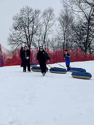 Three high honor roll students pull snow tubes over the snow on a cloudy afternoon at West Mountain.