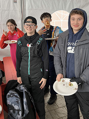 Students dressed in snow gear inside a tent smile for the camera. 