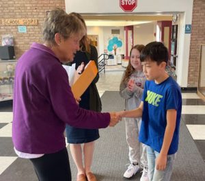 Elks officer shakes hands with an essay winner as another students and assistant principal stand nearby.