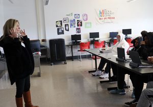 Side view of local business owner who appeared on TV's Shark Tank, standing at the front of the classroom animatedly speaking to students seated in the front row.