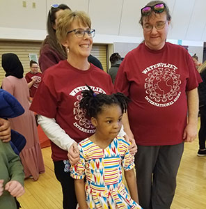 Teacher and teaching assistant stand with a student in brighlty printed dress  