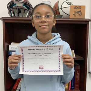 Grade 7 Student of the Month smiles at camera while holding Cannoneer Culture award certificate.