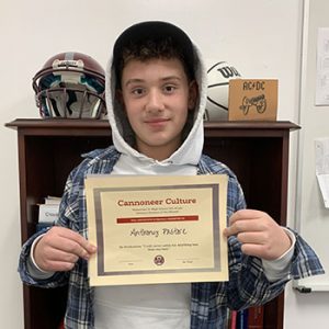 Grade 8 Student of the Month smiles at camera while holding Cannoneer Culture award certificate.