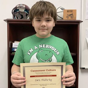 Grade 6 Student of the Month smiles at camera while holding Cannoneer Culture award certificate.