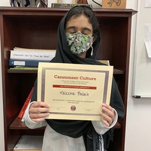Grade 7 Student of the Month smiles at camera while holding Cannoneer Culture award certificate.