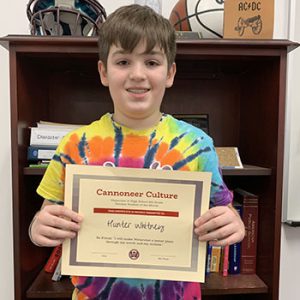 Grade 6 Student of the Month smiles at camera while holding Cannoneer Culture award certificate.