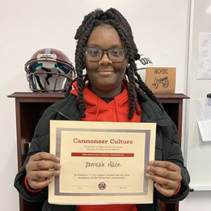 Grade 7 Student of the Month smiles at camera while holding Cannoneer Culture award certificate.