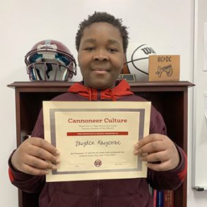 Grade 6 Student of the Month smiles at camera while holding Cannoneer Culture award certificate.