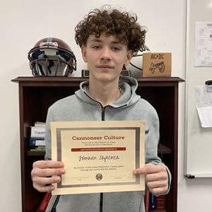 Grade 7 Student of the Month smiles at camera while holding Cannoneer Culture award certificate.