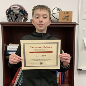 Grade 8 Student of the Month smiles at camera while holding Cannoneer Culture award certificate.