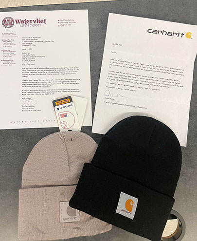 Student letter and company letter sit side by side on a desk with two Carhartt knit hats positioned below.