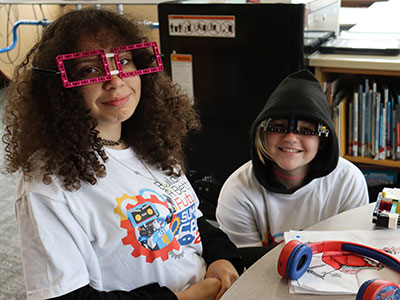 Two students wear eyeglasses made from Legos as they smile at the camera
