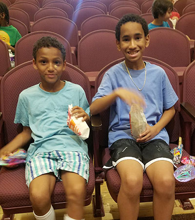 Two students seated in auditorium smiling and eating popcorn