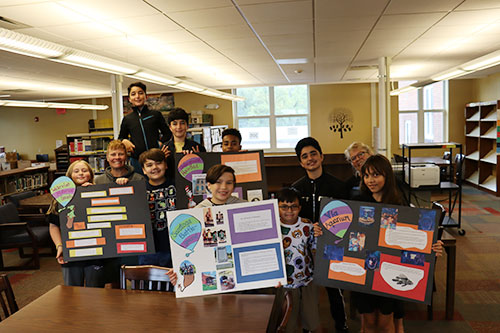 Group of students in travel program hold up poster boards with information about the sites they traveled to during the summer