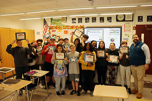 Grade 8 students  holding their achievement certificates stand together with their teacher and assistant principal