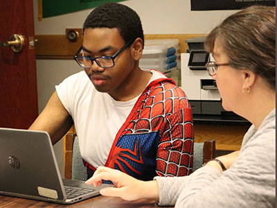A high school senior taps on a laptop keyboard to complete a college application with assistance from an HVCC admissions counselor. 