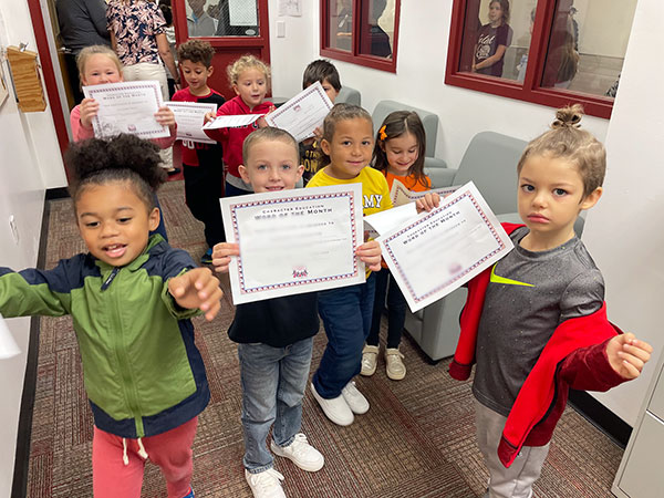 A small group of young elementary students smile at the camera after receiving their award certificates