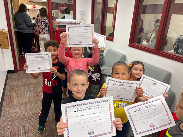 A small group of young elementary students smile at the camera after receiving their award certificates.