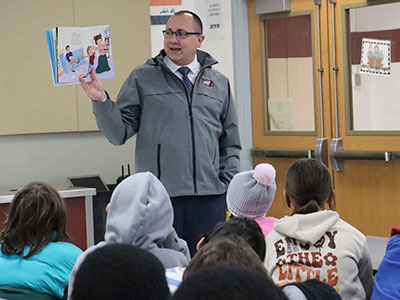 The superintendent holds up a book as he reads to students.